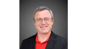 A headshot of Lubbock County Clerk candidate Jim Baxa, wearing a black blazer over a red polo shirt. He is sporting a smile that says, "I definitely know more about constitutional law than the Supreme Court," while staring directly into the camera with the confidence of a man who hasn't checked his spam folder for federal rulings since 2015.