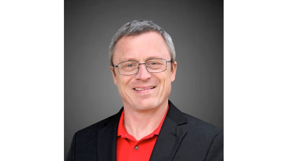 A headshot of Lubbock County Clerk candidate Jim Baxa, wearing a black blazer over a red polo shirt. He is sporting a smile that says, "I definitely know more about constitutional law than the Supreme Court," while staring directly into the camera with the confidence of a man who hasn't checked his spam folder for federal rulings since 2015.