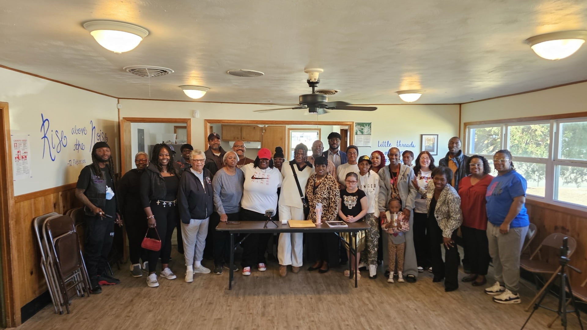 A group of approximately 25 community members, including representatives from the NAACP and the Lubbock Coalition of Black Democrats, stand together in a wood-paneled room for a press conference supporting student DeTayevion Lang.