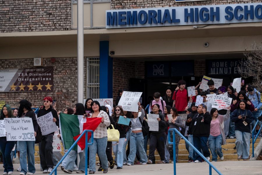 A large group of students at Memorial High School in San Antonio walking out of the building in protest. Several students are holding handmade signs with messages such as "No Decent Human Has a Heart Made of ICE" and "Gritamos por los que no pueden!" while one student prominently displays a Mexican flag.