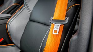 A close-up of a bright orange seat belt latched into a modern car seat, highlighting the safety features often debated by Lubbock drivers who miss the "freedom" of 1984.