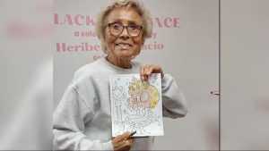 A medium shot of Billie Caviel, co-founder of the first Black-owned pharmacy in the U.S., smiling while holding up a colorful drawing of a crowned skull at the Caviel Museum of African American History in Lubbock.