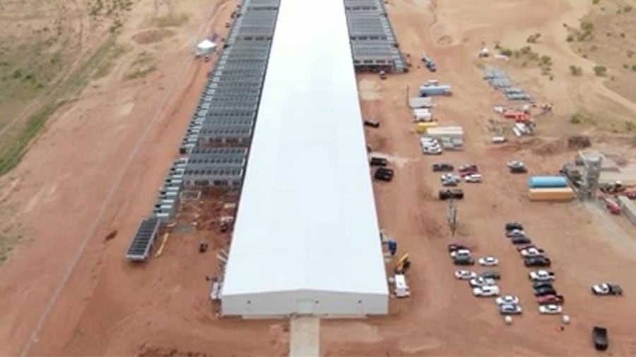 An aerial view of a massive, elongated white industrial building surrounded by dirt lots and parked trucks in the middle of the West Texas desert.