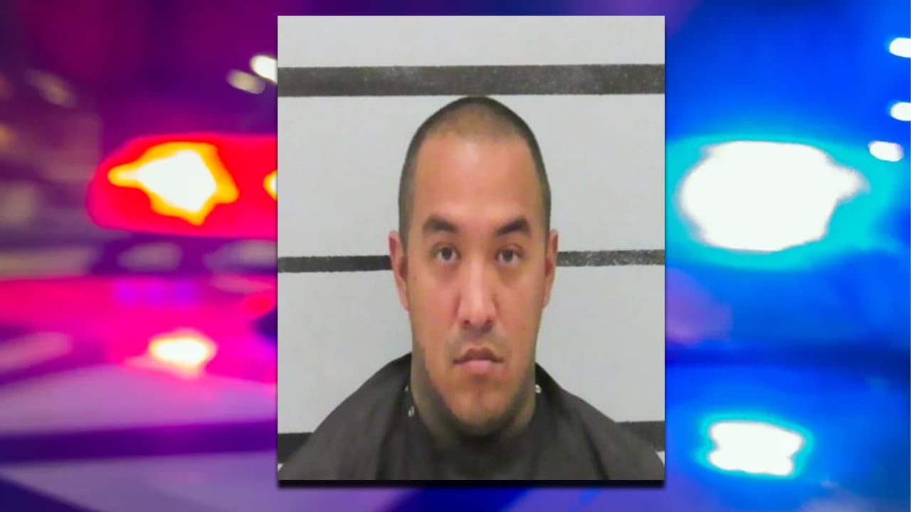 A mugshot of Christopher Roy Prieto, a 31-year-old man with short dark hair and visible neck tattoos, centered against a grey background with black horizontal measurement lines and flanked by a blurred background of police cruiser lights.