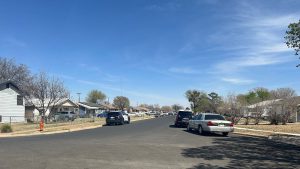 Lubbock Police SUVs parked on a residential street with one-story houses and clear blue skies during a shooting investigation.