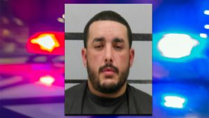 Mugshot of John Deleon with a blurred background of red and blue police lights.