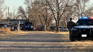 A Lubbock County Sheriff’s deputy stands by his patrol car with flashing lights on a gravel road, while a tactical SWAT vehicle and other law enforcement units converge on a property near FM 2641 during a narcotics search warrant operation.