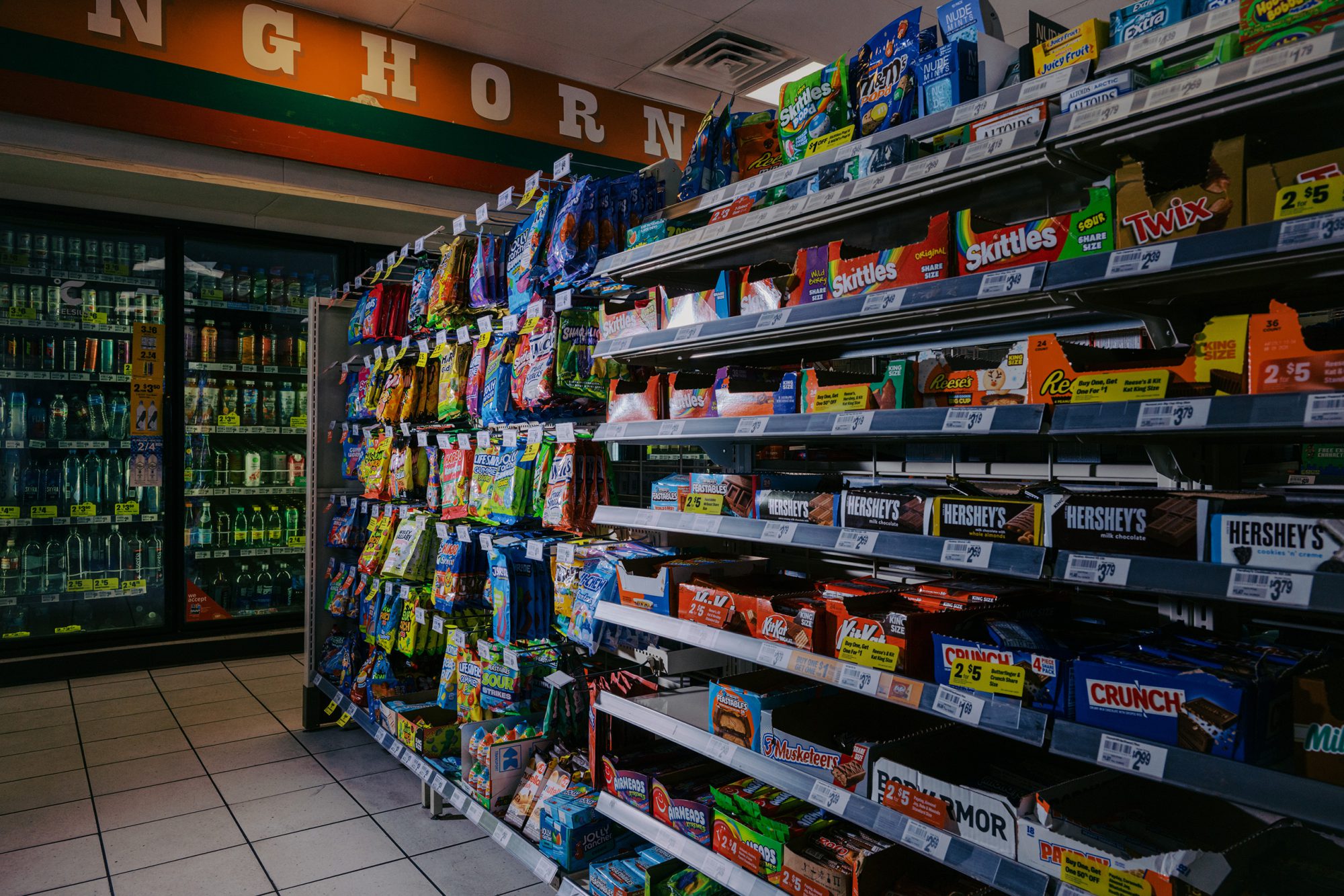 A brightly lit convenience store shelf packed with colorful candy bars and sodas that are now off-limits for SNAP recipients.