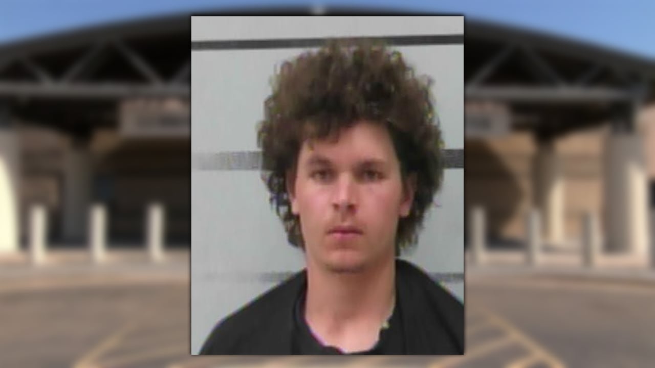A booking photo of Texas Tech freshman Jesse Rusinek, showing him with curly hair and a neutral expression against a grey, striped background.