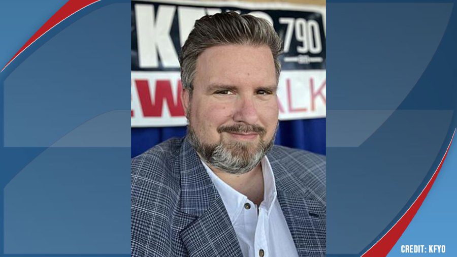 Late radio host Chad Hasty wearing a plaid blazer and smiling in front of a KFYO Newstalk radio banner.