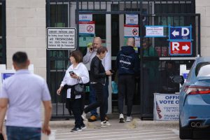 A group of frustrated voters standing outside a library polling location with signs pointing in opposite directions for Democrats and Republicans.