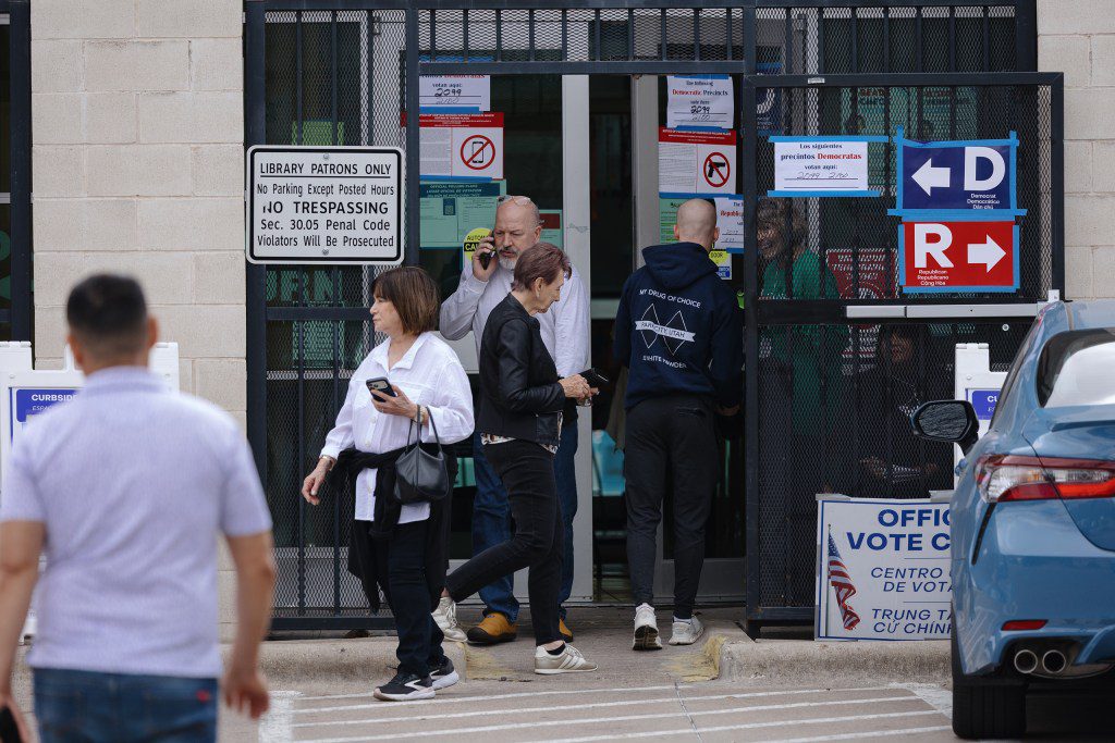 A group of frustrated voters standing outside a library polling location with signs pointing in opposite directions for Democrats and Republicans.