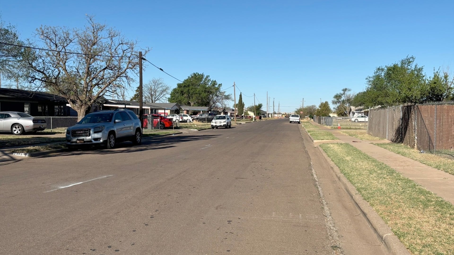A wide view of the 2400 block of East 8th Street in Lubbock, showcasing the charming mix of cracked pavement, chain-link fences, and the exact spot where a morning walk becomes a high-stakes survival game.