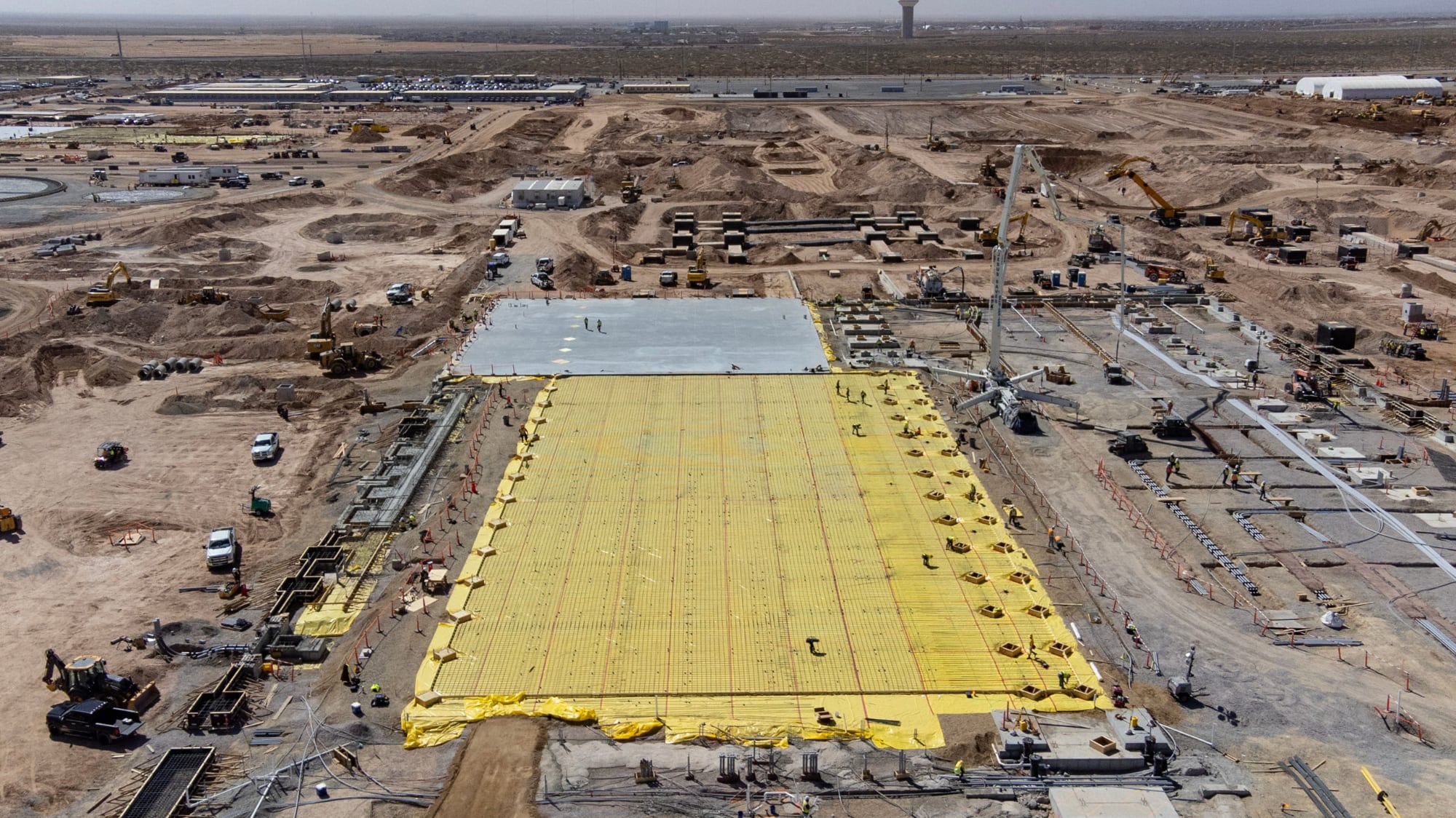 An aerial view of a massive, dusty construction site in the Texas desert where a sprawling yellow foundation is being laid for a data center that will eventually house more servers than the state has stable power lines.