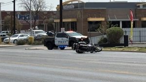 A crashed Lubbock Police motorcycle lying horizontally on the asphalt of 4th Street, perfectly positioned in front of a McDonald's to highlight the exact moment bravery met a "Do Not Pursue" order.