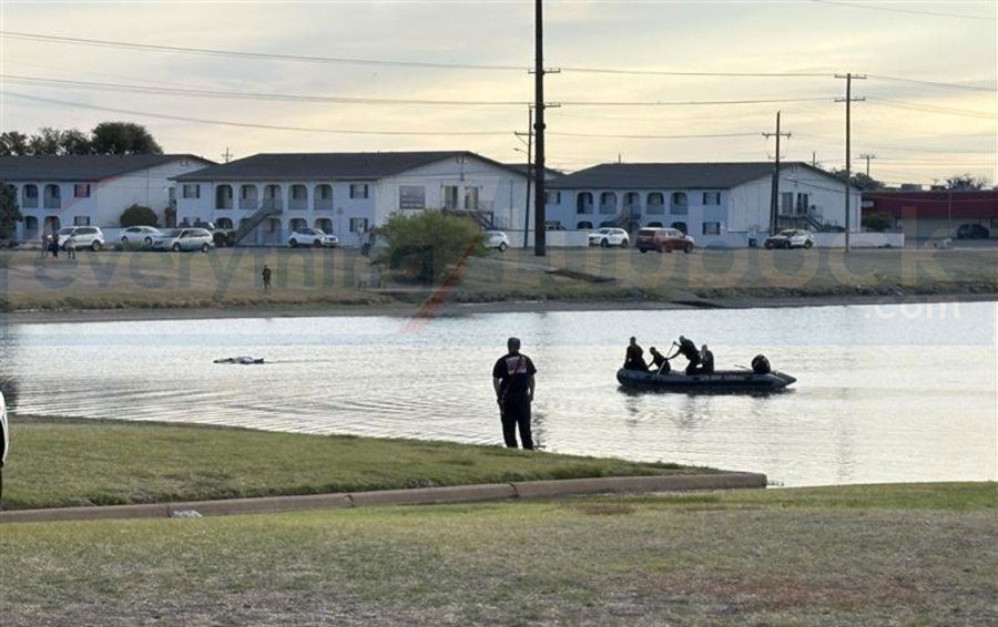 Lubbock Fire Rescue dive team in a small inflatable boat approaching a partially submerged vehicle in a murky playa lake.