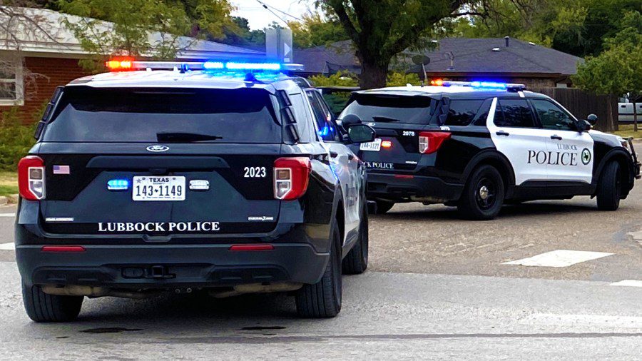 Two Lubbock Police Department SUVs with lights flashing, parked on a street near a residential neighborhood.