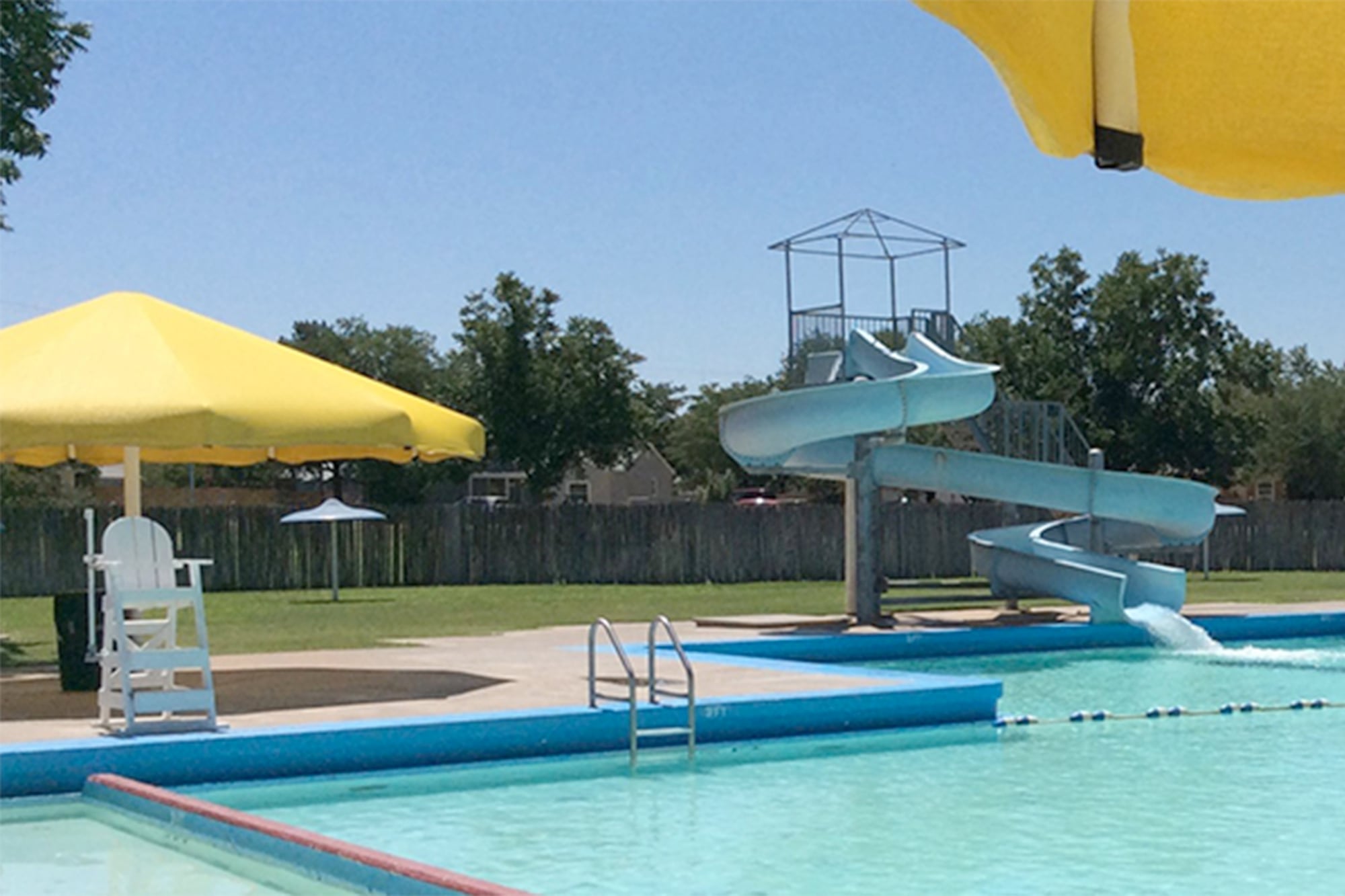 A rare historical photo of a Lubbock city pool actually containing water, featuring a blue slide and yellow umbrellas before the era of permanent closure.