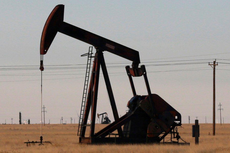 A silhouette of a rusty oil pumpjack operating in a dry, flat West Texas field under a dim sky.