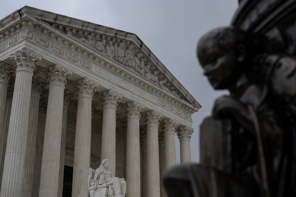 A low-angle shot of the U.S. Supreme Court building featuring the "Equal Justice Under Law" inscription with a blurred statue in the foreground.
