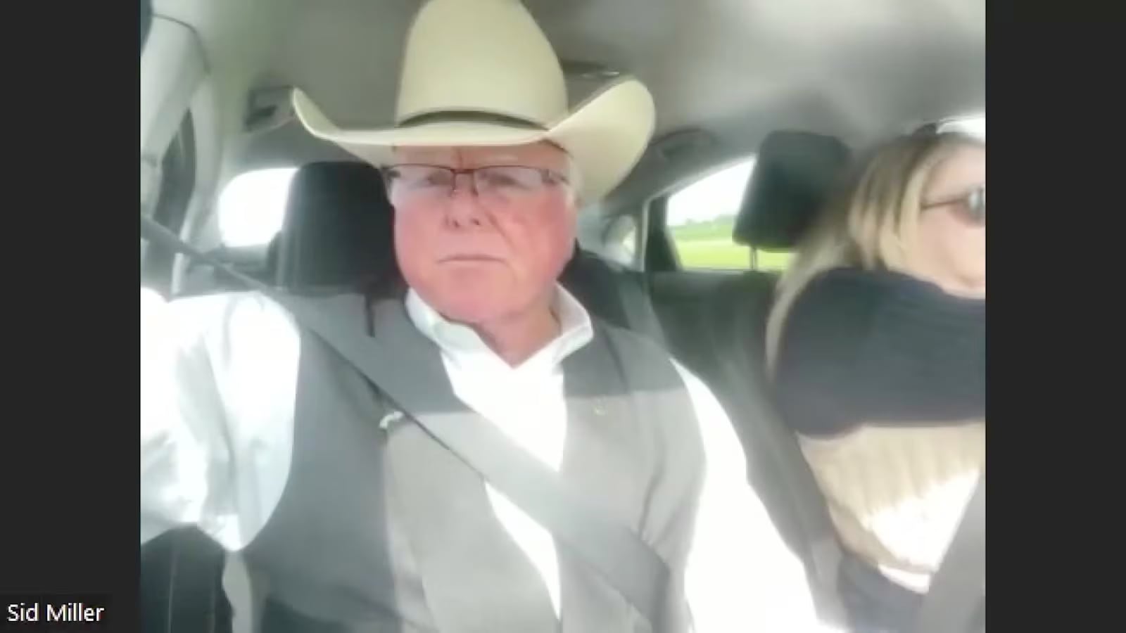 Texas Agriculture Commissioner Sid Miller wearing a cowboy hat and glasses while sitting in a car, looking sternly into a camera during a video call.