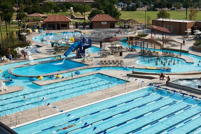 An aerial view of the expansive Texas Tech Leisure Pool featuring a lazy river, water slide, and lap pools under a bright Lubbock sun.