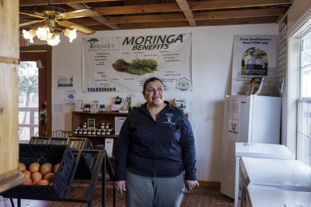 Diana Padilla standing in her farm office in Harlingen, Texas, surrounded by educational posters about Moringa and agriculture.