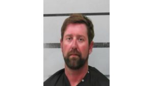 Booking mugshot of Casey Nickelson, a 39-year-old man with brown hair and a beard, standing in front of a white background with black horizontal lines.