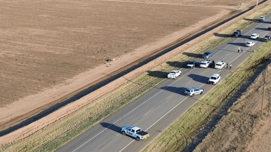 An aerial view of multiple police cruisers and emergency vehicles blocking a two-lane rural Texas highway next to a barren, flat dirt field.