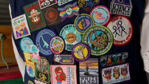 A close-up of a Girl Scout vest heavily decorated with colorful merit patches for camping, wildlife, and cookie volunteering.