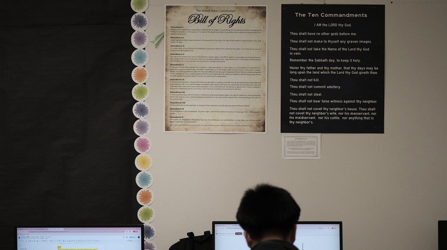 A classroom wall displaying a Ten Commandments poster and the Bill of Rights side-by-side above computer monitors.