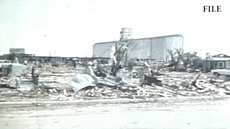 A grainy black-and-white archival photo showing the widespread destruction of the 1970 Lubbock tornado, with flattened homes in the foreground and a large grain elevator standing in the distance.