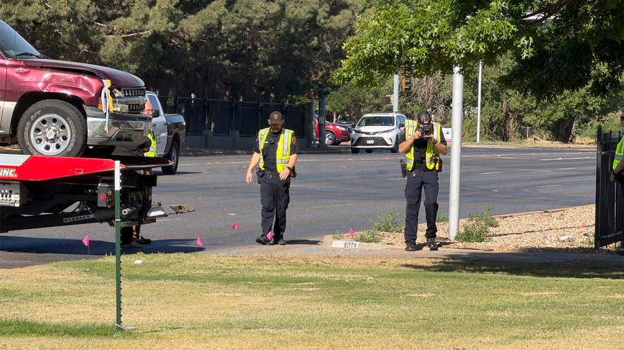 Police investigators in high-visibility vests examine a crash scene on 19th Street featuring a damaged red pickup truck on a flatbed tow truck.