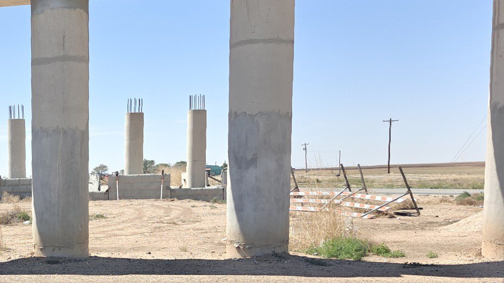 Unfinished concrete bridge pillars for the US 87 and FM 41 overpass standing in a barren, dusty construction site south of Lubbock.