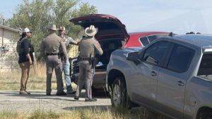 Texas Department of Public Safety troopers and law enforcement officers standing next to a red SUV with an open trunk and a gray pickup truck on the side of Idalou Highway after a police pursuit.