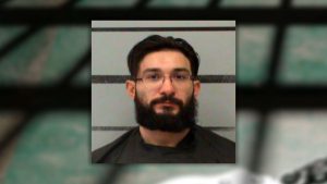Mugshot of Mark Landreth, a 32-year-old man with dark hair, glasses, and a thick beard, posing against a gray law enforcement height chart.