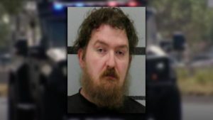 Mugshot of Derrick Karl Green featuring a disheveled beard and messy brown hair against a gray law enforcement background.