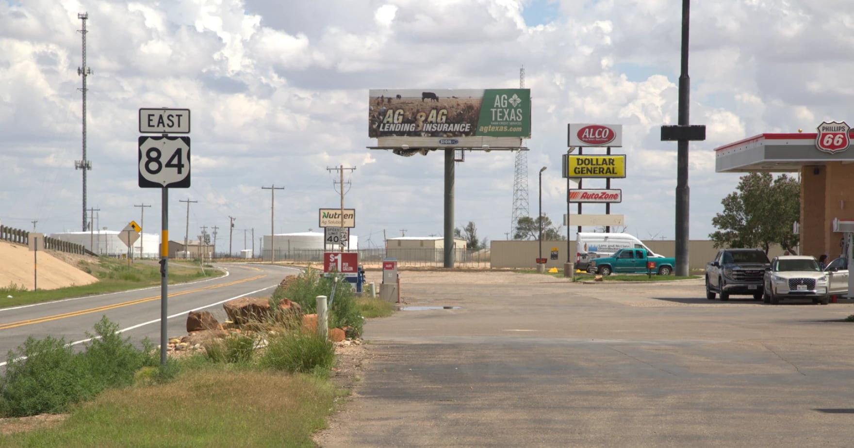 A view of Highway 84 East in rural West Texas, featuring a Phillips 66 gas station, local commercial signs for Dollar General and AutoZone, and an Ag Texas billboard under a vast sky.