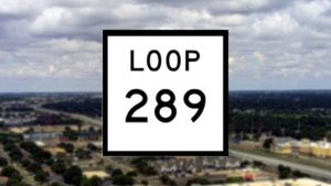 A close-up of a white square Texas highway sign with bold black lettering that reads "LOOP 289", superimposed over a blurry aerial view of Lubbock's flat landscape, roads, and residential areas under a cloudy sky.