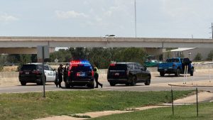 Multiple Lubbock Police Department SUVs with flashing lights and a blue pickup truck stopped on an access road near a highway overpass.