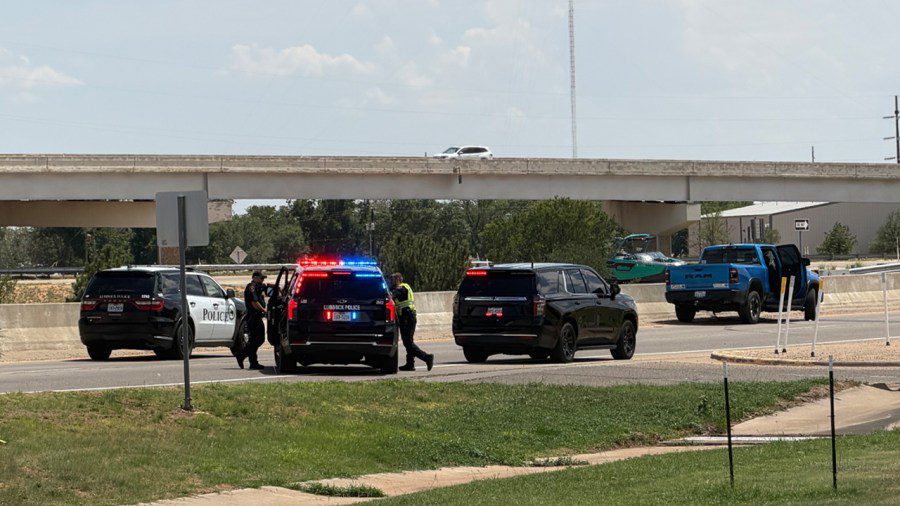 Multiple Lubbock Police Department SUVs with flashing lights and a blue pickup truck stopped on an access road near a highway overpass.