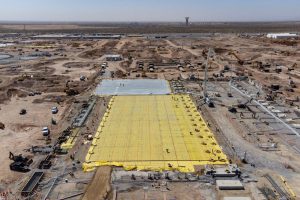 An aerial view of the Meta Platforms data center complex under construction on a massive 1,000-acre site in far Northeast El Paso, near the Texas-New Mexico state line. The image shows heavy machinery, cranes, concrete foundations, and a large grid section covered in yellow vapor barrier sheets, captured on March 12, 2026.
