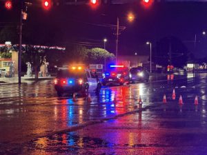Multiple Lubbock police SUVs with flashing red and blue lights blocking a wet, reflective city street at night with orange traffic cones scattered across the pavement.