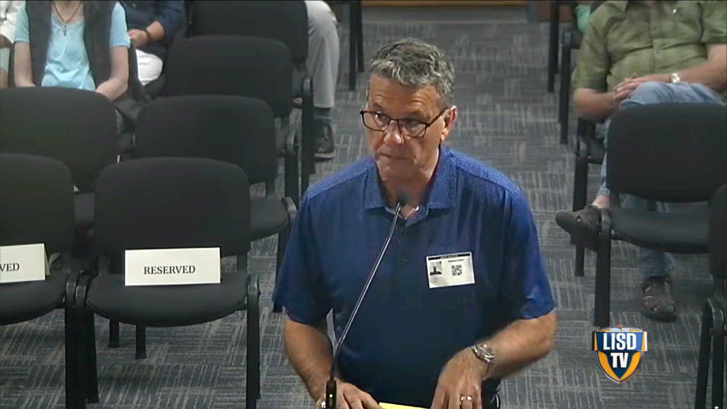 State Senator Charles Perry speaking at a microphone during a Lubbock ISD school board trustee meeting.