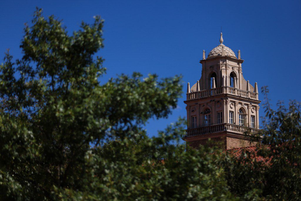 The Spanish Renaissance tower of the Texas Tech University Administration Building framed by tree branches in Lubbock, Texas.